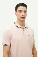 Chomba de piqué color rosa claro, de corte clásico, con cuello y mangas con ribete a rayas en blanco, gris y negro. Tiene tapeta de dos botones y logo bordado en el pecho.
