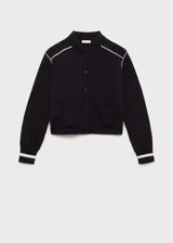 Chaqueta negra de punto con corte bomber, cierre frontal con botones a presión, bolsillos laterales y ribete blanco en cuello, puños, ruedo y hombros.