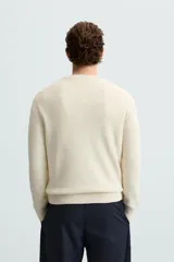 Jersey color crema de punto perlado, con cuello redondo, manga larga y corte regular fit.