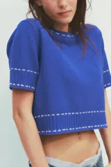 Top azul de tejido de punto con cuello redondo y manga corta. Detalle de pespuntes blancos a contraste en cuello, mangas y ruedo.