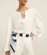 Blusa blanca de poliéster satinado, con mangas largas abullonadas, cuello con abertura en forma de gota y lazo con colgantes de corazón.