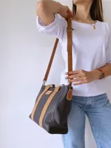 Cartera negra de cuero con forro de tela, doble asa corta color camel y correa larga desmontable también color camel.