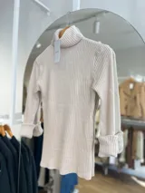 Polera blanca de tejido de punto acanalado, con cuello alto y mangas largas con puños acampanados.