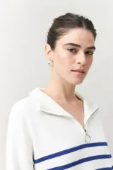 Polera blanca de punto con cuello alto y cierre metálico, de calce relajado y diseño a rayas horizontales azules.