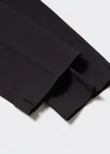 Pantalón negro de corte skinny y largo cropped, confeccionado en tejido fluido con forro interior. Presenta tiro medio, trabillas, bolsillos laterales y traseros de ribete. Cierre frontal con cremallera y botón.