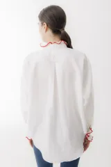 Camisa blanca de lino con cuello mao, manga larga abullonada y puños con detalle de crochet rojo. Tiene bolsillo de crochet en el pecho y cierre frontal con botones de madera.