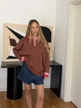 Buzo marrón de algodón con cuello polo rosa y puños acanalados rosas con rayas rojas.