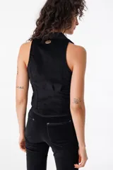 Chaleco de pana color borgoña, ajustado al cuerpo con pinzas y elásticos en la zona baja de la espalda. De largo irregular (más largo delante que atrás), cuello camisero clásico y cierre frontal con ganchos peleteros.