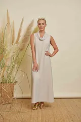 Vestido largo sin mangas, color beige claro con brillo sutil, cuello drapeado y corte recto.