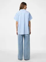 Camisa de popelina con mangas cortas y cuello clásico. Presenta cierre frontal de botones y diseño estampado de rayas verticales blancas y celestes.