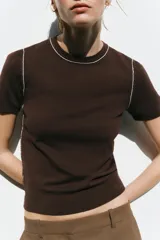 Top de punto color marrón con cuello redondo y manga corta. Detalle de ribete blanco en cuello y mangas.