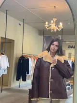 Abrigo marrón de cuero con cuello y borde de piel sintética color crema y cierre con botones.