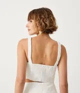 Blusa cropped blanca de lino con escote en V y tirantes trenzados.
