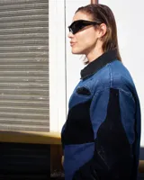 Camisa de denim azul y negro con cortes curvos y simétricos, cierre frontal de alpaca y cuello en cuero vacuno. Incluye bolsillos delanteros con bordado del logo Temblad.