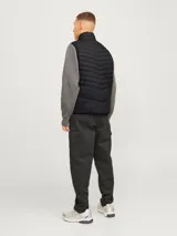 Chaleco acolchado negro sin mangas con cuello alto y cierre lateral oculto y cremallera frontal. Bolsillos frontales y diseño plegable para fácil almacenamiento. Relleno de fibra sintética para calidez ligera.