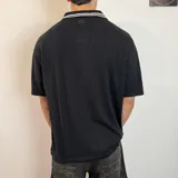 Chomba negra tejida con cuello tipo polo, mangas cortas con rayas blancas y logo estampado en el pecho.