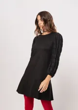 Vestido negro de cuello redondo, con mangas largas tipo globo y terminación elástica, confeccionado en dos telas combinadas.
