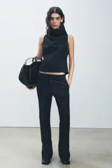 Pantalón negro de tiro medio con cintura con trabillas y corte flare. Cierre frontal con cremallera, botón y gancho metálico.