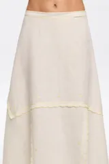 Falda midi color blanco hueso de algodón y lino, con corte irregular y vuelo. Presenta cierre lateral invisible y bordados a contraste en costuras y bajos.