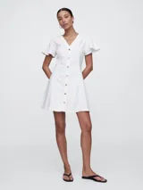 Vestido corto de denim blanco, corte fit and flare, con cuello en V, mangas cortas con volados y cierre frontal con botones.