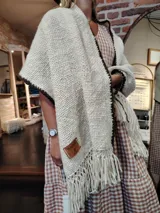 Chal tejido a mano en lana merino color crudo, con flecos y borde tejido en marrón oscuro. Diseño con textura de canasta.