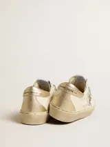 Championes de cuero Golden Goose modelo Hi Star, color blanco con detalles en dorado y plateado. Presentan una estrella de glitter plateado en el lateral, puntera de gamuza gris y talón en cuero dorado. La suela de plataforma incluye inscripciones de la marca y un acabado sutilmente desgastado.