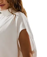 Remera estilo polo blanca de corte amplio con cuello clásico y botonadura corta en el frente. Tiene mangas cortas con dobladillo y aberturas laterales en el ruedo.