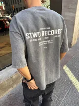 Remera gris de algodón pesado con efecto lavado. Estampa en la espalda con texto "Introducing STWD Records 00 000 P&B 0091 EST 0 9 Entertainment Co. Superior Sound Quality Bhe Dig".
