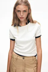 Remera corta de punto fino color blanco, de ajuste entallado con cuello redondo, mangas cortas y terminaciones acanaladas.