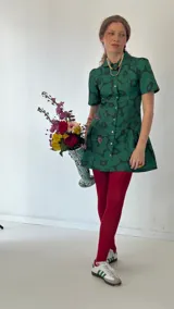 Vestido corto verde con estampado de flores negras, cuello camisero, mangas cortas abullonadas y falda con volantes.