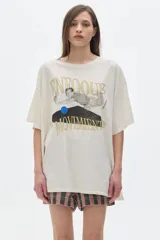 Remera unisex color crudo, de cuello redondo y manga corta, con estampado frontal de una figura humana y texto en dorado.