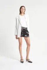 Short sastrero negro con estampado floral, de brocado laminado, con alforzas en el frente, bolsillos delanteros, pinzas traseras y bolsillo ojal. Tiene snaps y botón interno, y forrería de satén negra.