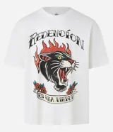 Remera color crema de corte recto, con cuello redondo y mangas cortas. Presenta un estampado estilo tatuaje con un felino en llamas y la frase "Redención es una virtud".