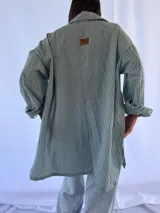 Camisa oversize a rayas verticales azules y blancas, con cuello clásico y cierre frontal con botones.