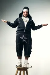 Campera negra de algodón impermeable con doble capucha, una de ellas tipo pasamontañas. Presenta viras y logos reflectivos, y cierres de metal. La parte trasera tiene un estampado de estrella con tachas.