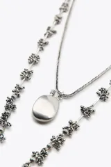 Set de dos collares plateados: uno con eslabones de piezas metálicas rectangulares y circulares, y otro con cadena fina y dije en forma de botella.