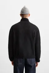 Cárdigan negro de punto con cuello subido, manga larga, bolsillos de vivo en cadera, acabados en rib y cierre frontal con cremallera.