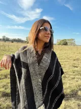 Ruana tejida a mano en telar, confeccionada en lana Merino color negro con detalles en blanco y flecos blancos.