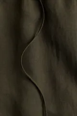 Pantalón verde militar de corte holgado en tejido liviano de mezcla de lino. Modelo de tiro alto con cintura elástica y cordón para ajustar fino, bolsillos laterales discretos y piernas rectas.