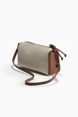 Bandolera rectangular de tela color beige con textura tipo canasta y detalles en cuero marrón. Tiene cierre superior con cremallera, correa larga regulable con hebilla y forro interior.