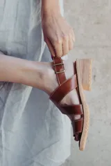 Sandalias de cuero color marrón con tiras cruzadas, taco de 4cm y cierre con hebilla metálica ajustable en el tobillo.