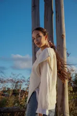 Chaleco tejido color crudo con aplique de cuero marrón en el cuello y detalle de pespunte en el contorno.