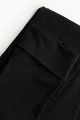 Pantalón negro de punto suave, con cintura ancha plegable y corte acampanado.