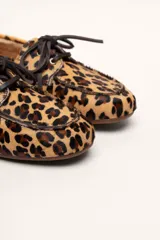 Mocasín tipo boat shoe con estampado de vaca en tonos marrón y blanco, confeccionado en cuero. Cuenta con cordones de cuero marrón oscuro y suela de goma.
