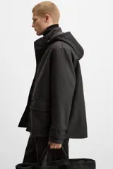 Parka negra de corte regular, confeccionada en tejido técnico acolchado. Tiene cuello alto con capucha ajustable, mangas largas con puños ajustables, bolsillos con solapa en la cadera y un bolsillo interior. El cierre frontal es con cremallera oculta por solapa con botones a presión.