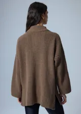 Sweater marrón de punto con cuello polo, cierre de cremallera parcial y parche bordado en el pecho.