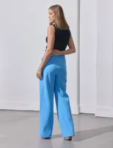 Pantalón largo de crepe elastizado color verde, de corte recto, con bolsillos delanteros y apliques de botones metálicos.