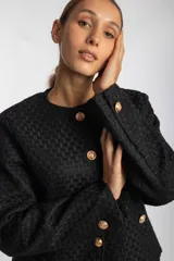 Chaqueta negra con textura, cuello redondo, cierre frontal con botones dorados y bolsillos delanteros con solapa y botón dorado.