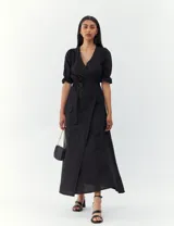 Vestido negro de corte midi, con escote en V cruzado, mangas 3/4 con elástico en los puños y lazo en la cintura.