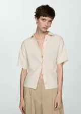 Camisa color crema de lino con cuello camisero, manga corta y cierre frontal con botones.